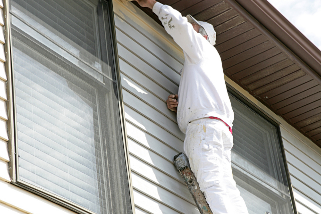 Exterior house painter on a ladder painting top side of the wall.