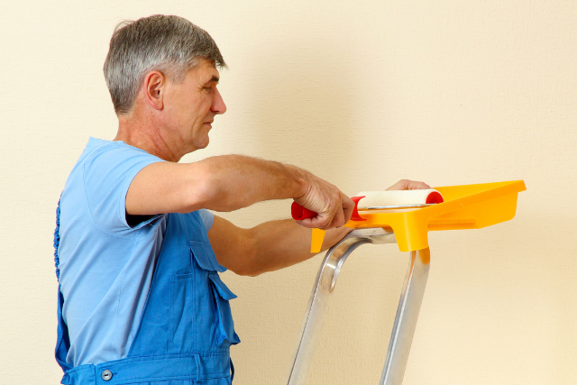 Painter paints wall in room with a small ladder